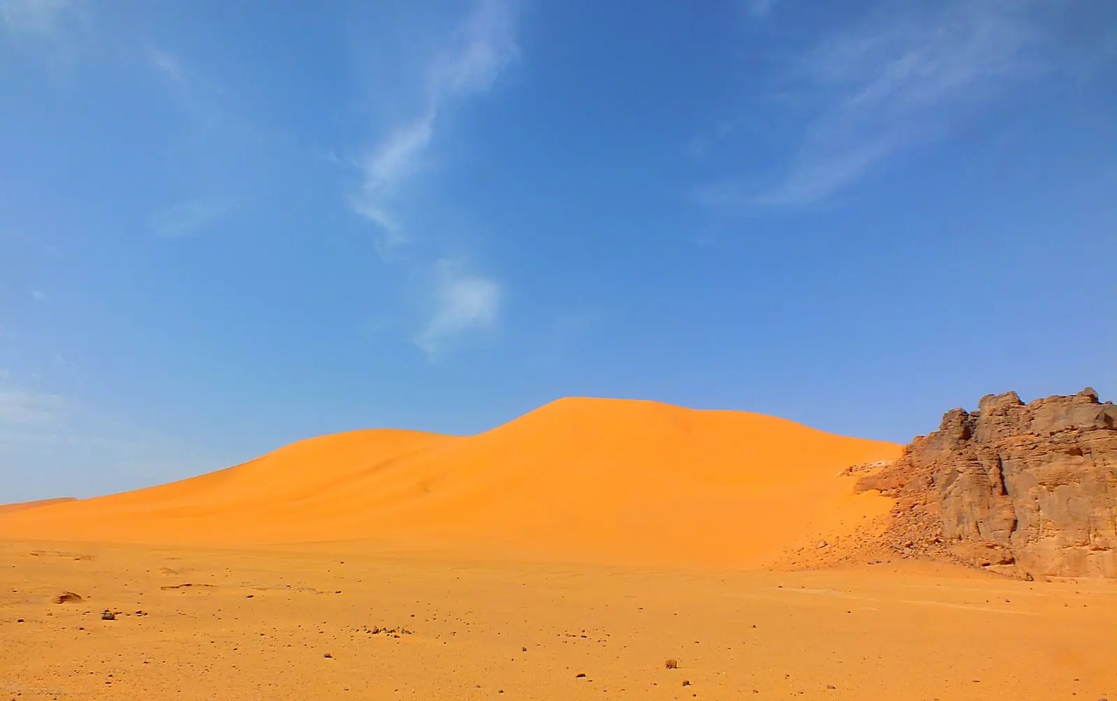 Orange klitter og en brun klippeformation under blå himmel i Tassili n'Ajjer i Sahara