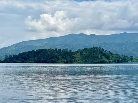 Skovklædt ø i den blanke Kivu-sø foran grønne bjerge under hvide skyer, set fra Bukavu
