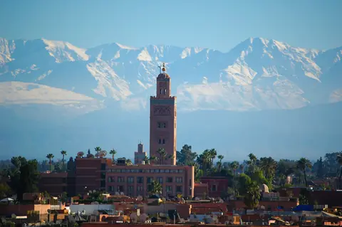 Koutoubia-moskéens minaret rejser sig over Marrakechs tage og palmer foran det sneklædte Atlasbjerg