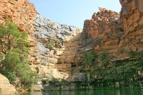 Grønt vand i bunden af en kløft med høje, lagdelte sandstensvægge ved Guelta Maya i Ennedi
