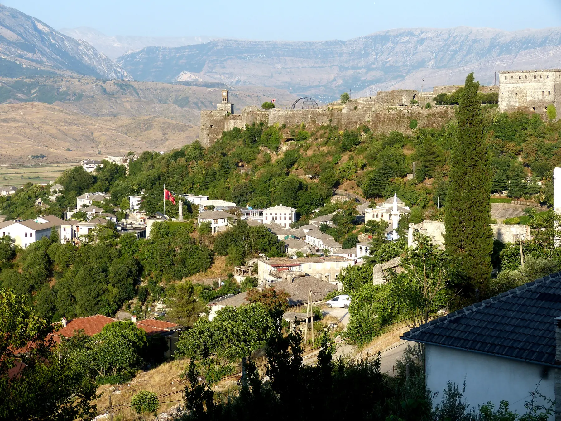 Gjirokastërs stenhuse på bakkeskråningen under borgen med bjerge i baggrunden i det sydlige Albanien