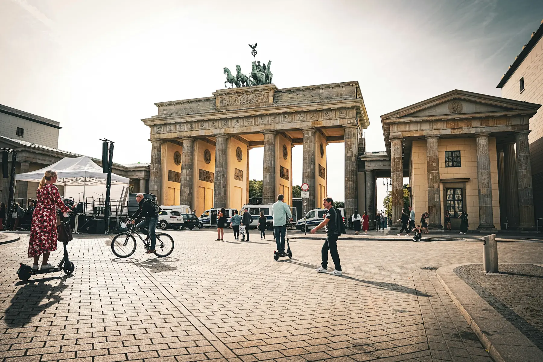 Brandenburger Tor i Berlin på en solrig dag med fodgængere, cyklister og løbehjul på den brolagte plads foran