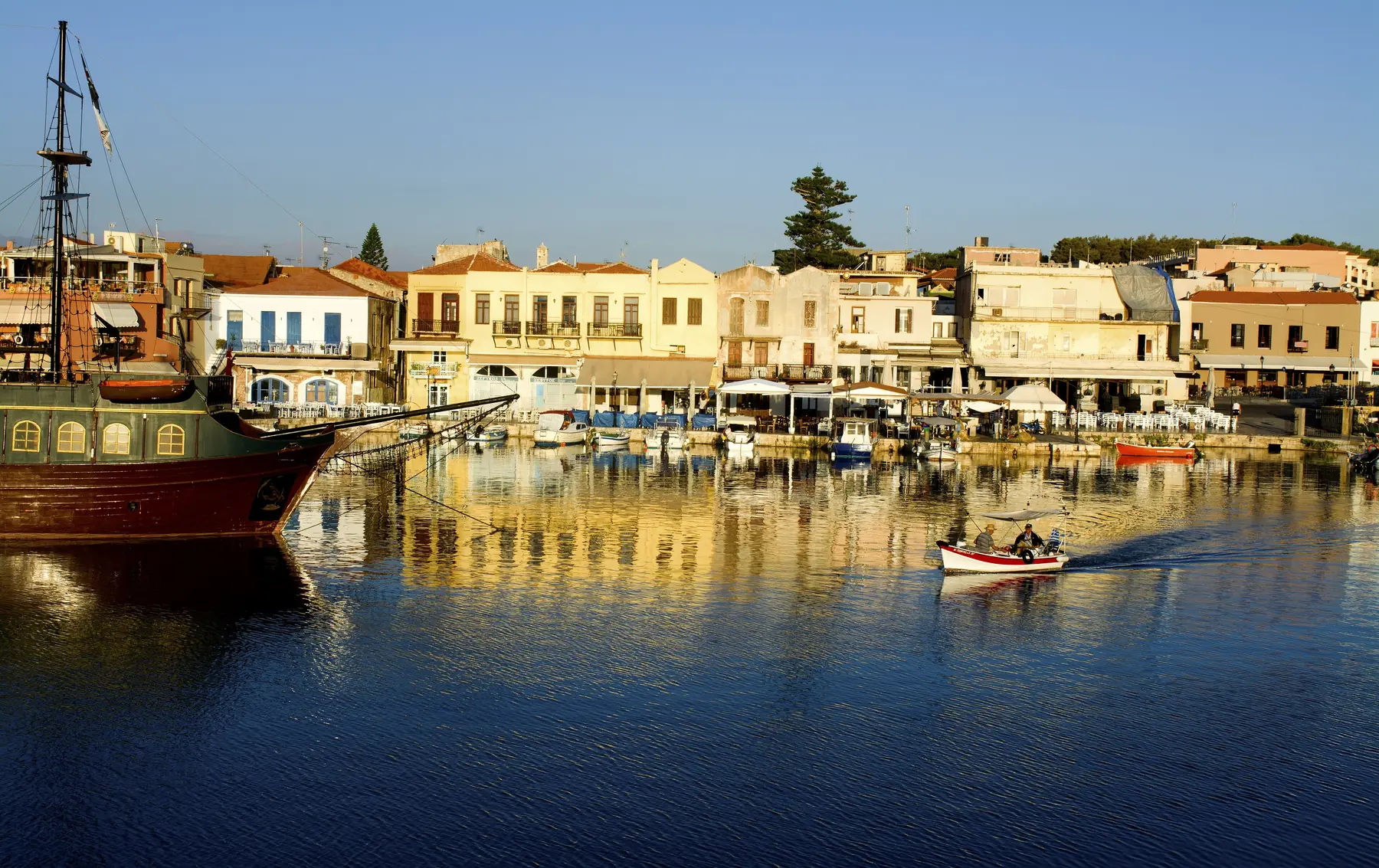 Huse og et gammelt sejlskib spejler sig i den venetianske havn i Rethymno på Kreta i morgenlys