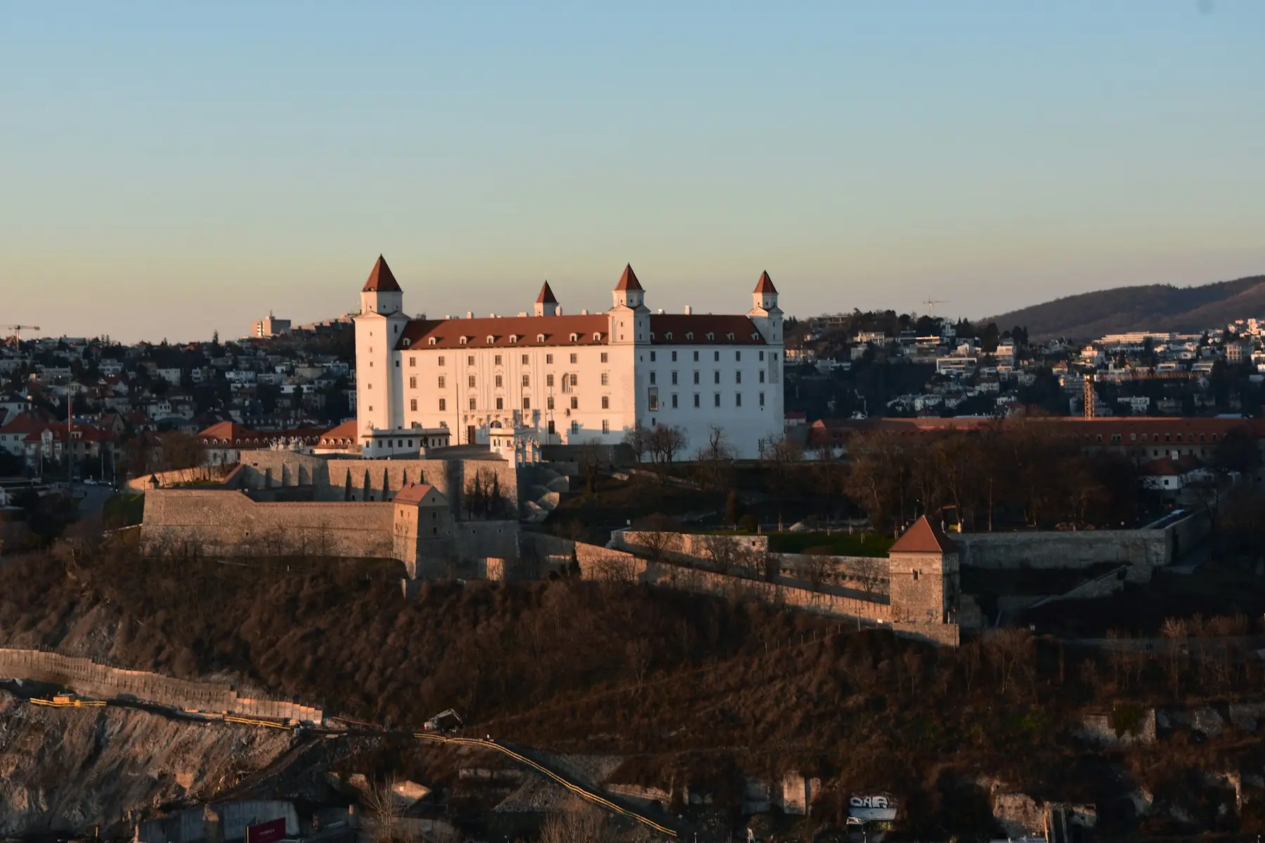 Det hvide slot i Bratislava med fire hjørnetårne på bakken over byen i aftensol