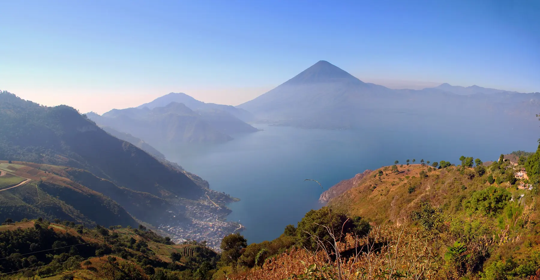 Atitlán-søen i Guatemala med vulkanen Atitlán og stejle grønne bjergsider i morgenlys
