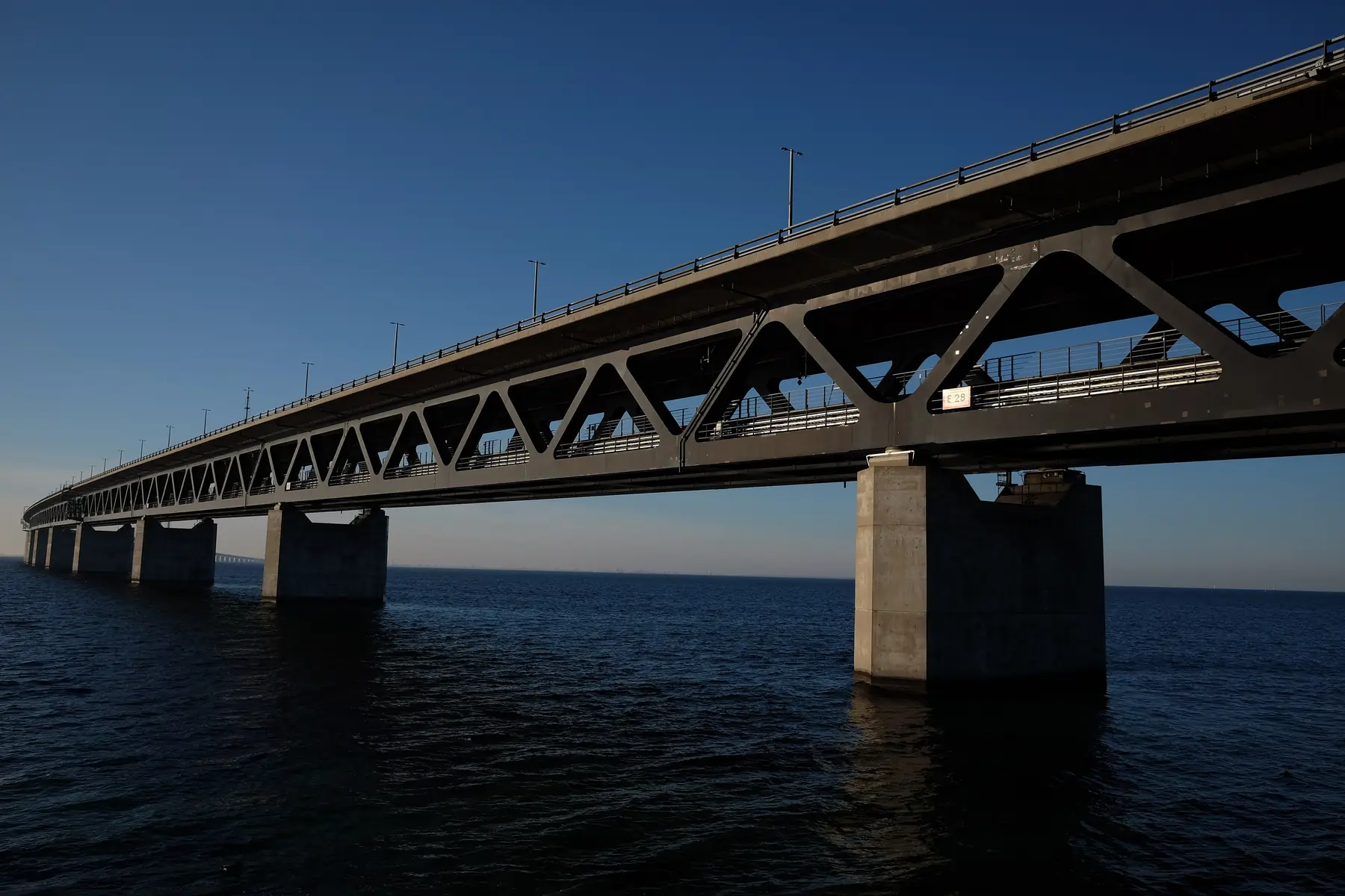 Øresundsbroens stålkonstruktion og betonpiller over mørkeblåt vand i klart aftenlys