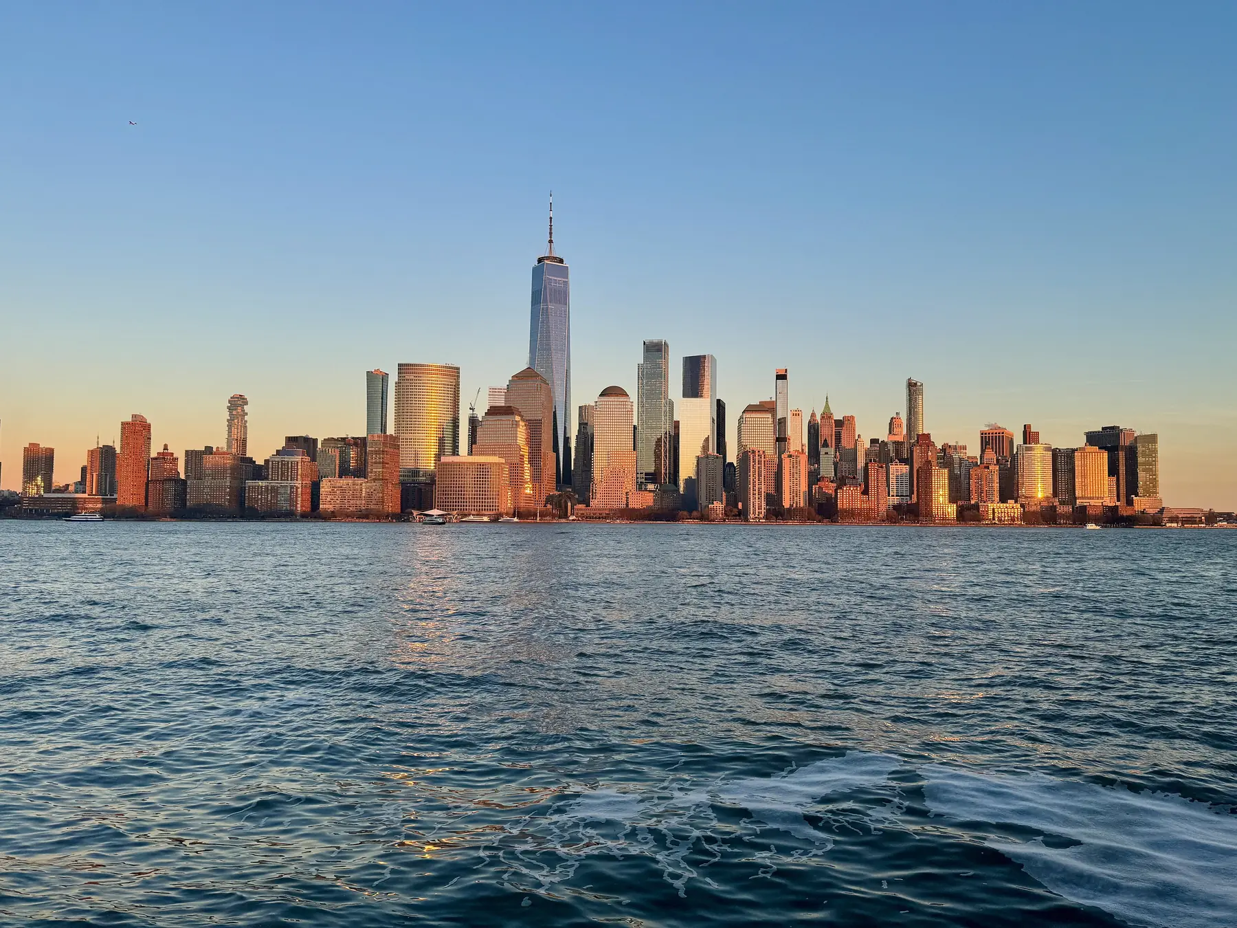 Lower Manhattans skyskrabere med One World Trade Center i gyldent aftenlys set fra vandet i New York