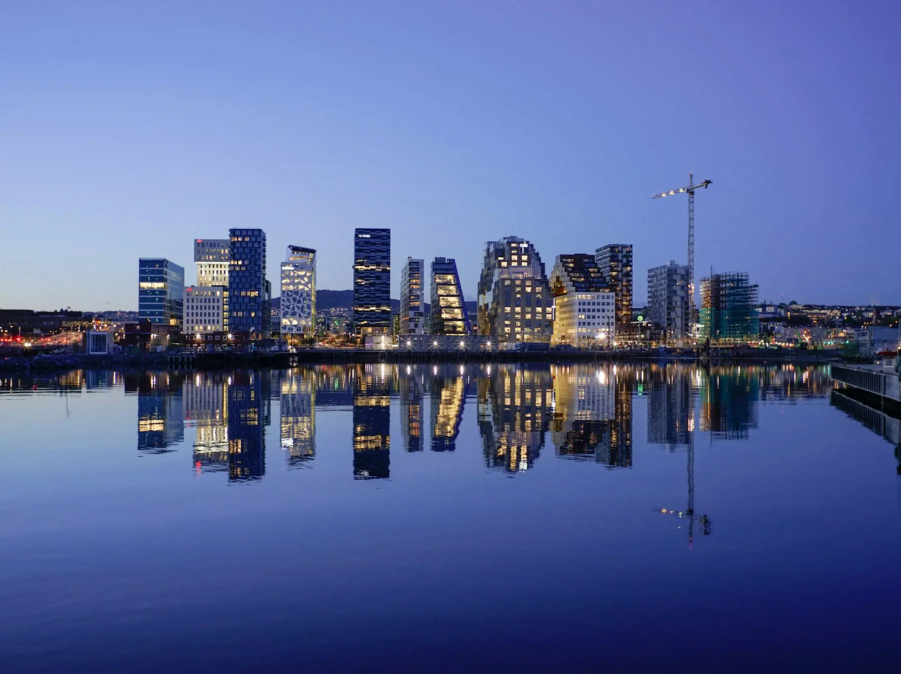 Højhusene i Bjørvika i Oslo oplyst i den blå time og spejlet i det stille vand i havnen