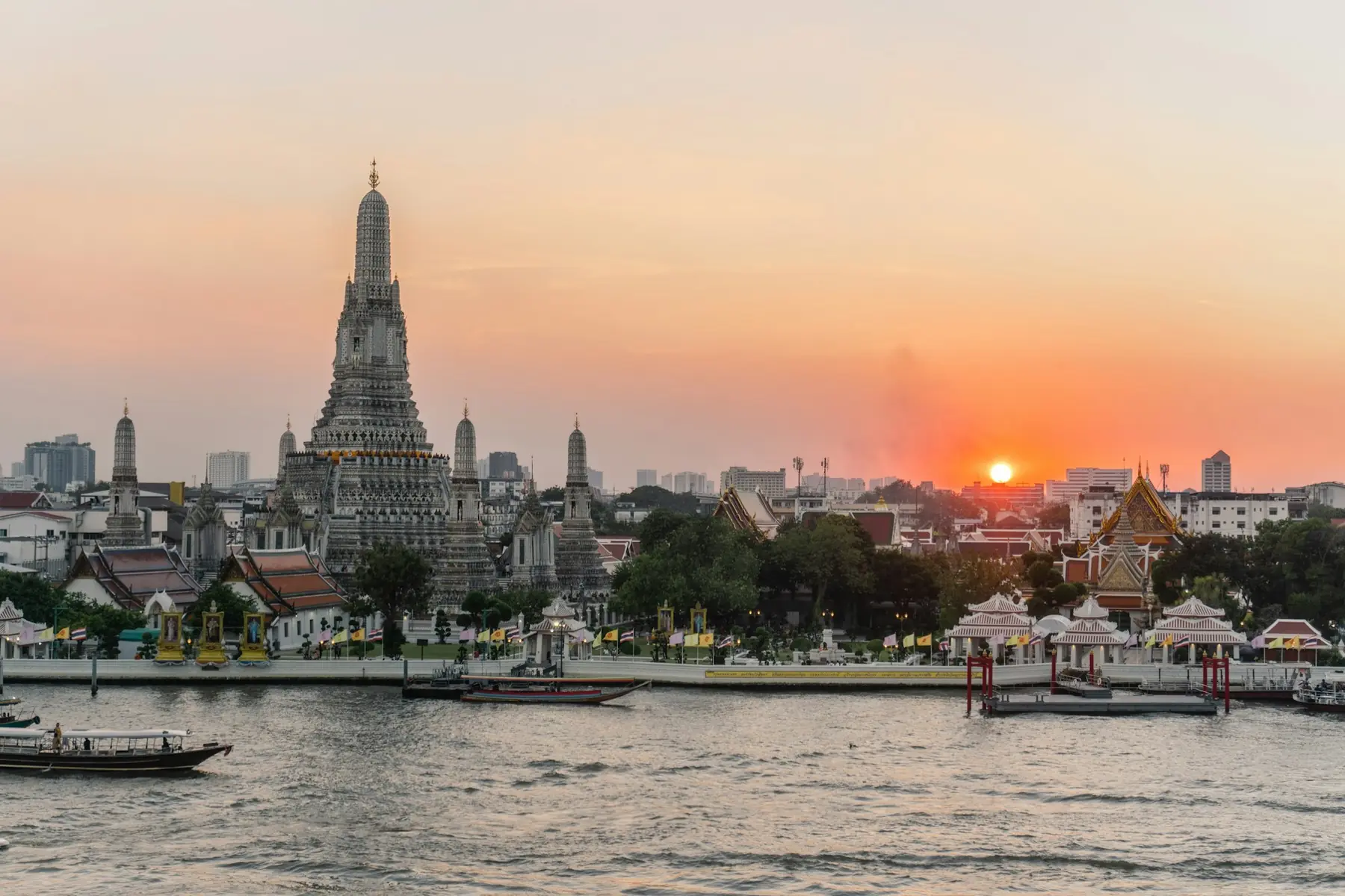 Templet Wat Arun ved Chao Phraya-floden i Bangkok med solnedgang over byen og både på vandet