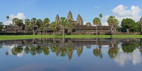 Angkor Wats tempeltårne og palmer, der spejler sig i en stille dam under blå himmel