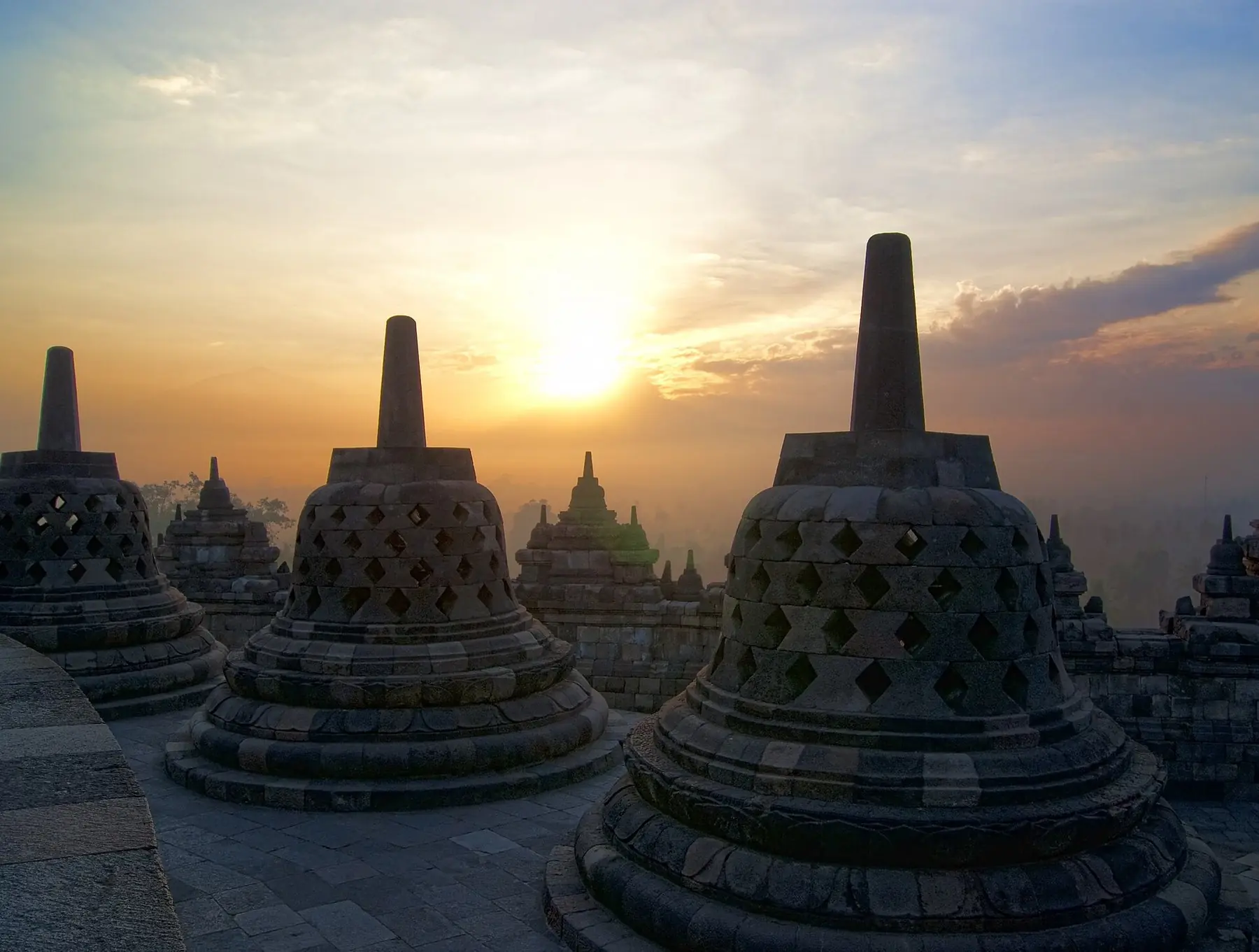 Klokkeformede stenstupaer på templet Borobudur i solopgangens gyldne lys på Java