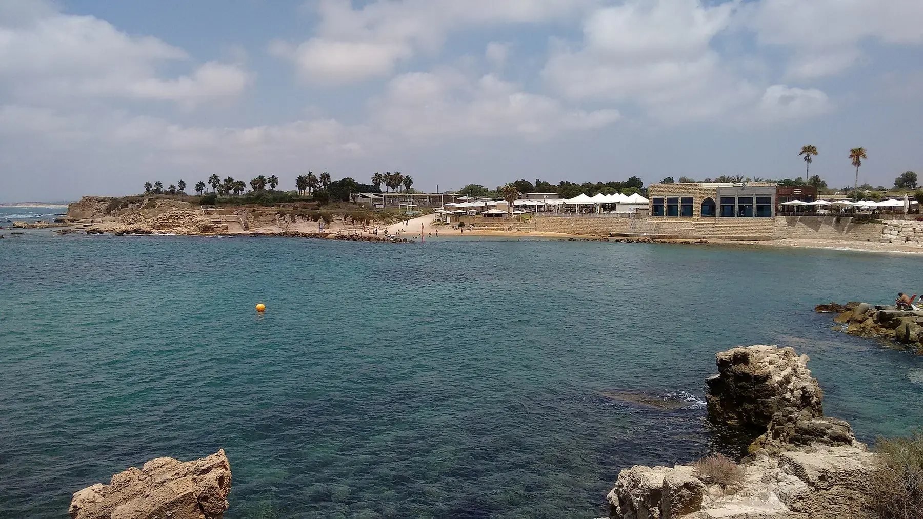 Turkis middelhavsbugt med klipper og den gamle havn i Caesarea under lyse skyer
