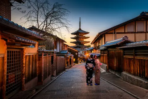 To kvinder i kimono på en brolagt gade med gamle træhuse og Yasaka-pagoden i Kyoto ved solnedgang