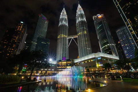 De oplyste Petronas-tårne i Kuala Lumpur om aftenen med farvede springvand i forgrunden