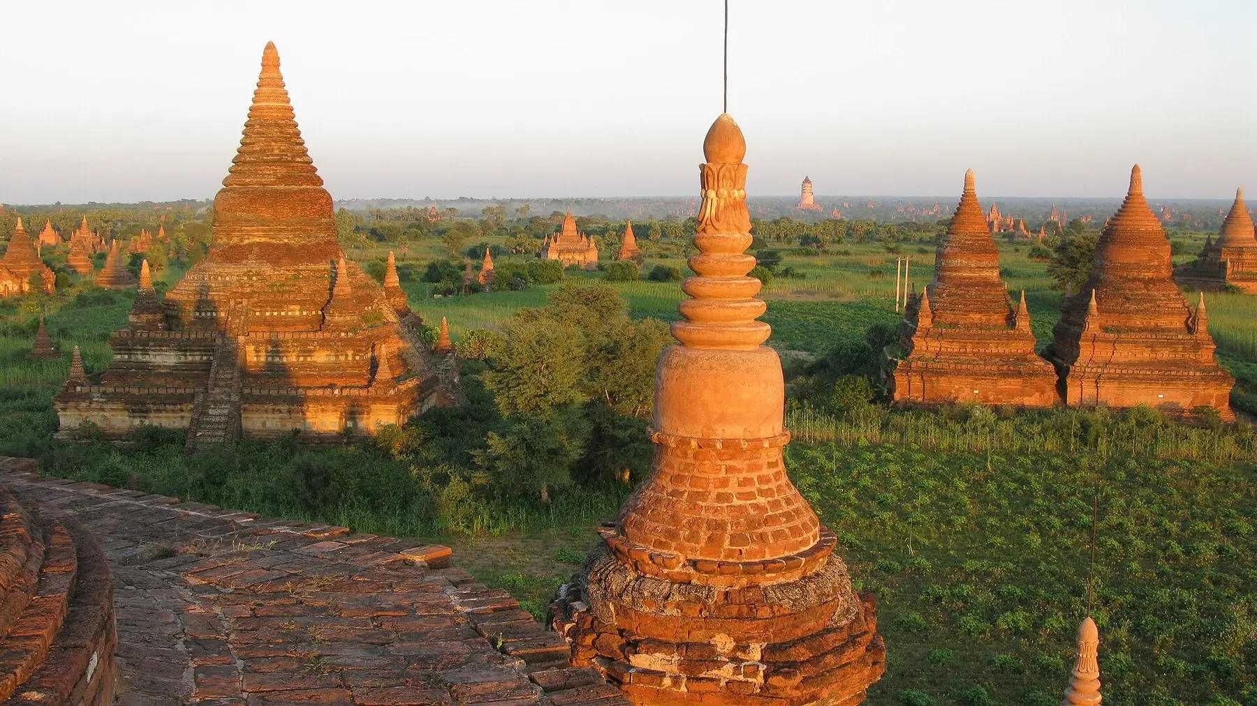 Teglstensstupaer og templer, der lyser orange i aftensolen over sletten i Bagan