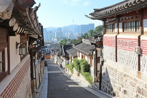 En smal gade med traditionelle hanok-huse i Bukchon i Seoul med højhuse og N Seoul Tower i baggrunden