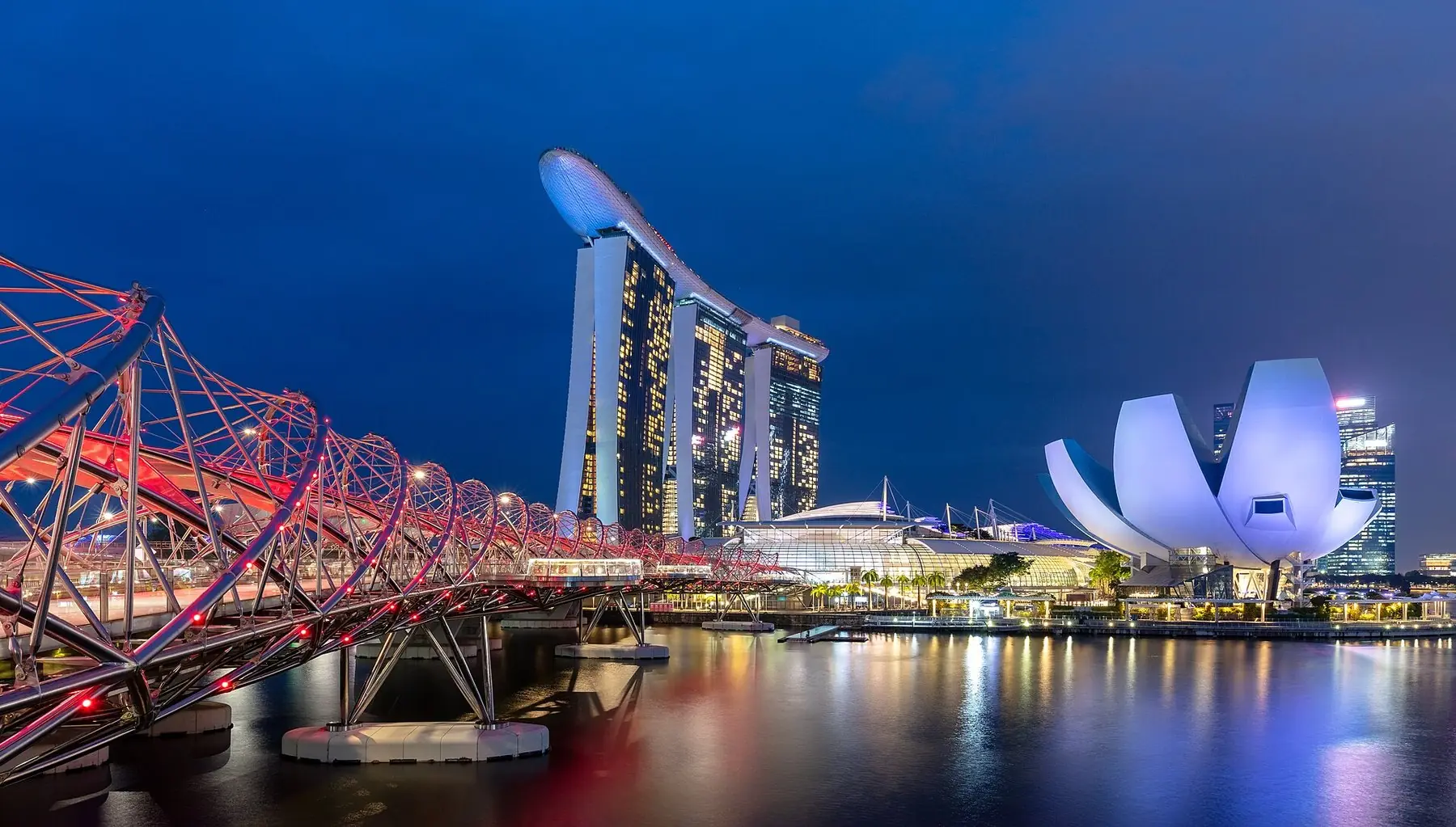 Den oplyste Helix-bro, hotellet Marina Bay Sands og det lotusformede museum ved Marina Bay i den blå time