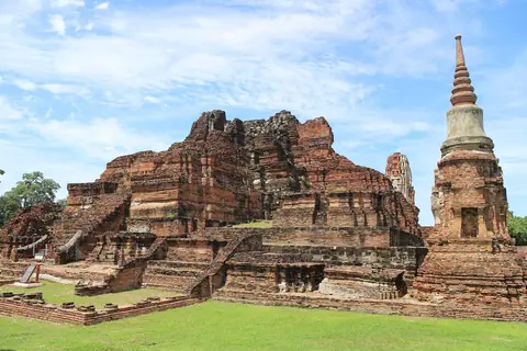 Ruiner af teglstenstempler og en hvid stupa på en græsplæne i Wat Mahathat i Ayutthaya