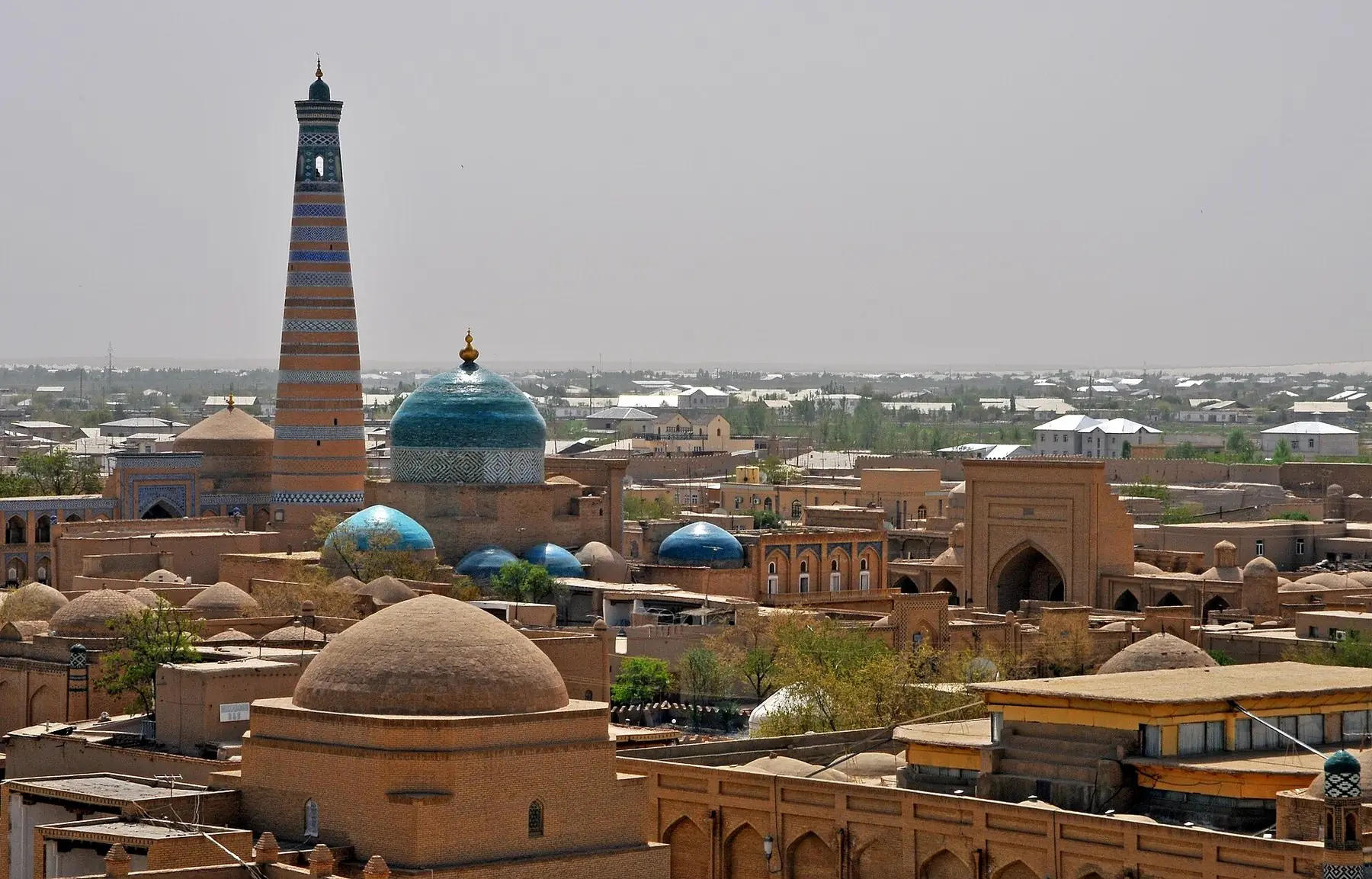Den gamle bydel Itchan Kala i Khiva med turkise kupler og en høj stribet minaret, set fra citadellets tag