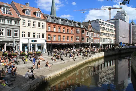 Folk sidder på trappen ved åen langs Åboulevarden i Aarhus en solskinsdag