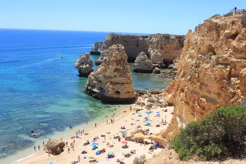 Gyldne klipper, klippestøtter og en badestrand med parasoller ved Praia da Marinha i Algarve