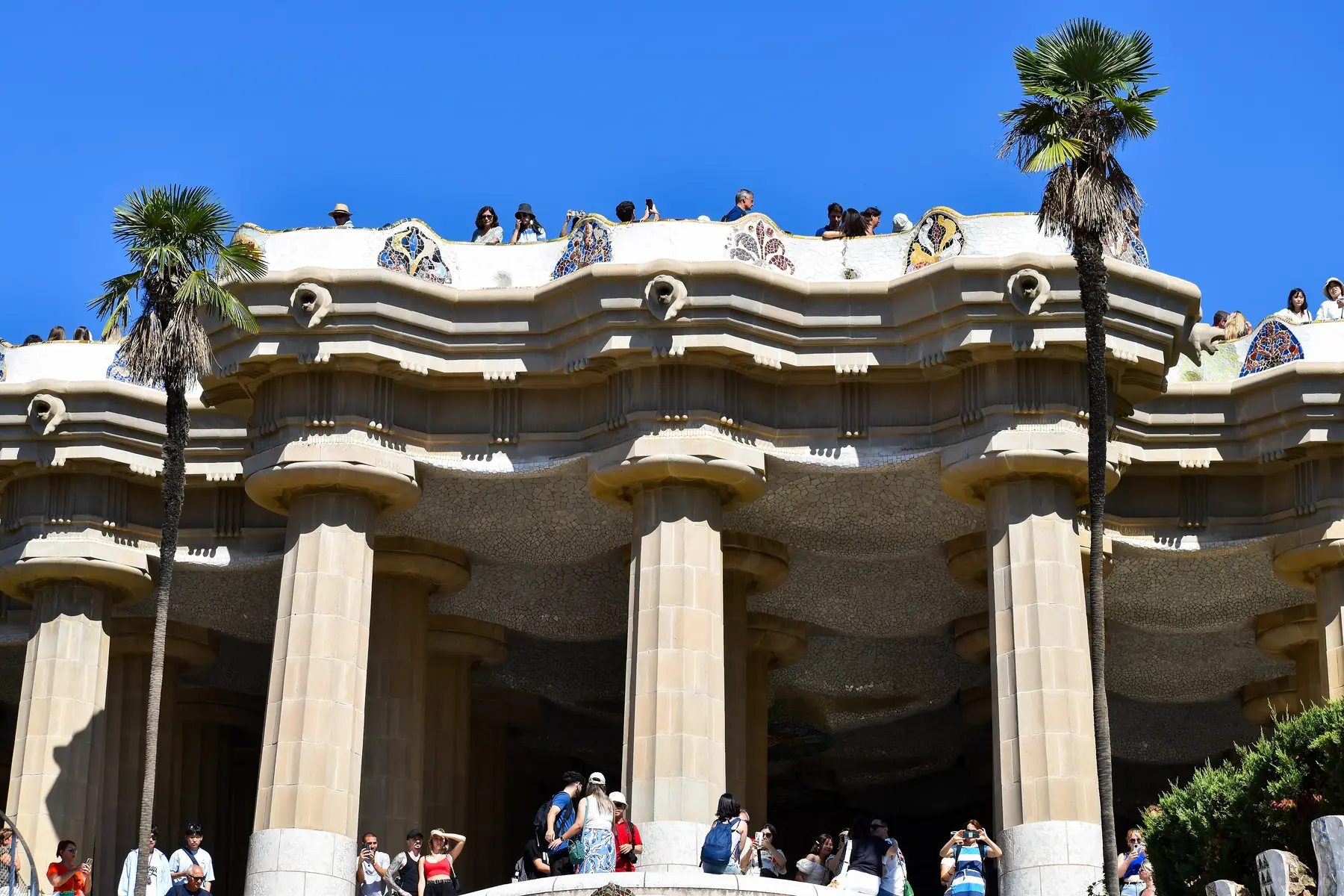 Søjlegangen under terrassen i Gaudís Park Güell i Barcelona med palmer og besøgende