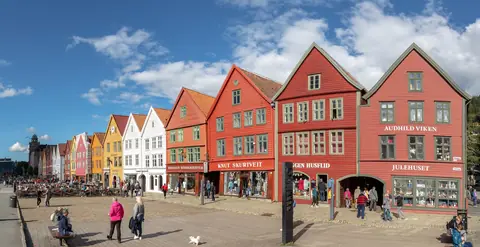 De farverige træhuse på Bryggen i Bergen med turister på kajen en solskinsdag