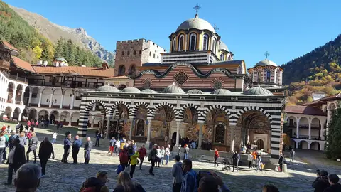 Rila-klostrets stribede kirke med kupler i gården, omgivet af klosterbygninger og skovklædte bjerge