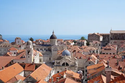 Røde tegltage, klokketårnet og domkirkens kuppel i Dubrovniks gamle by set fra bymuren med havet bagved