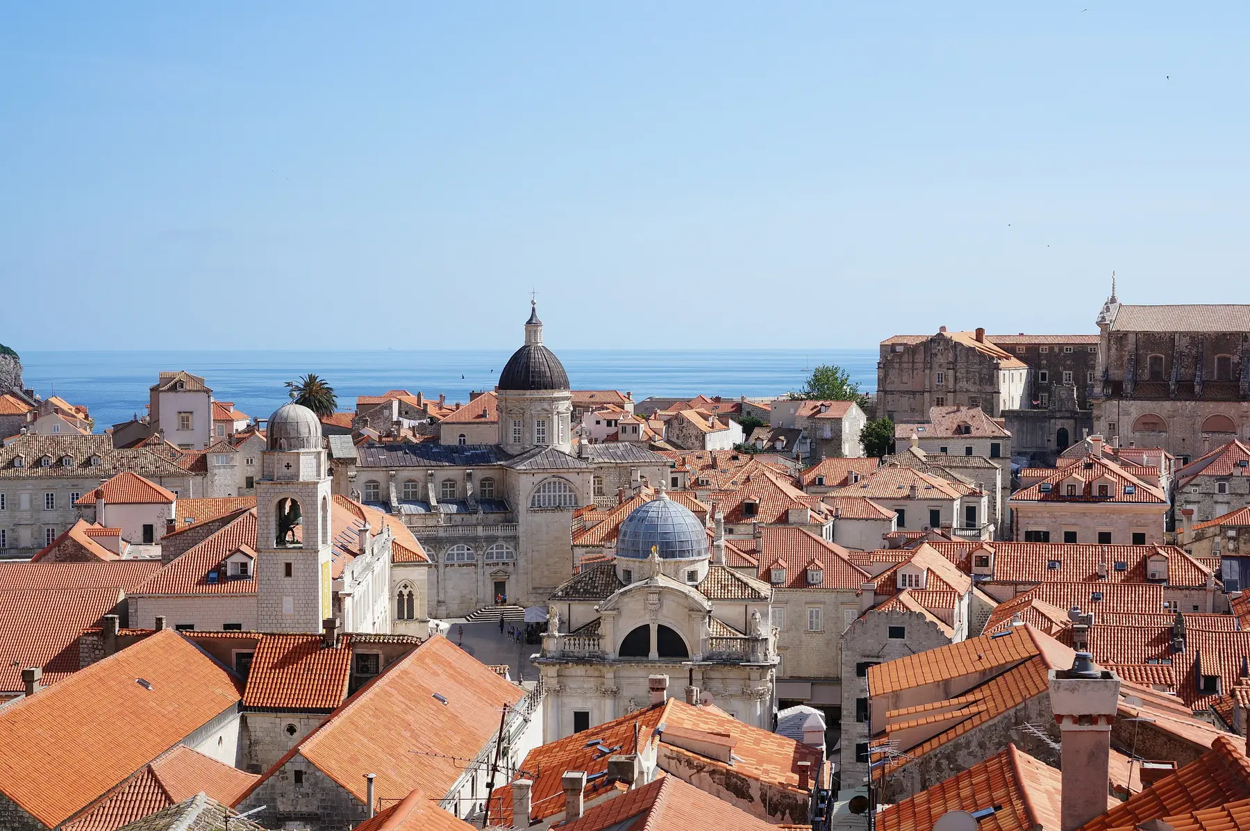 Røde tegltage, klokketårnet og domkirkens kuppel i Dubrovniks gamle by set fra bymuren med havet bagved