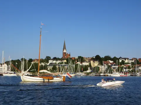 Et gammelt sejlskib og lystbåde på Flensborg Fjord foran Jürgensby og St. Jürgen-kirkens spir