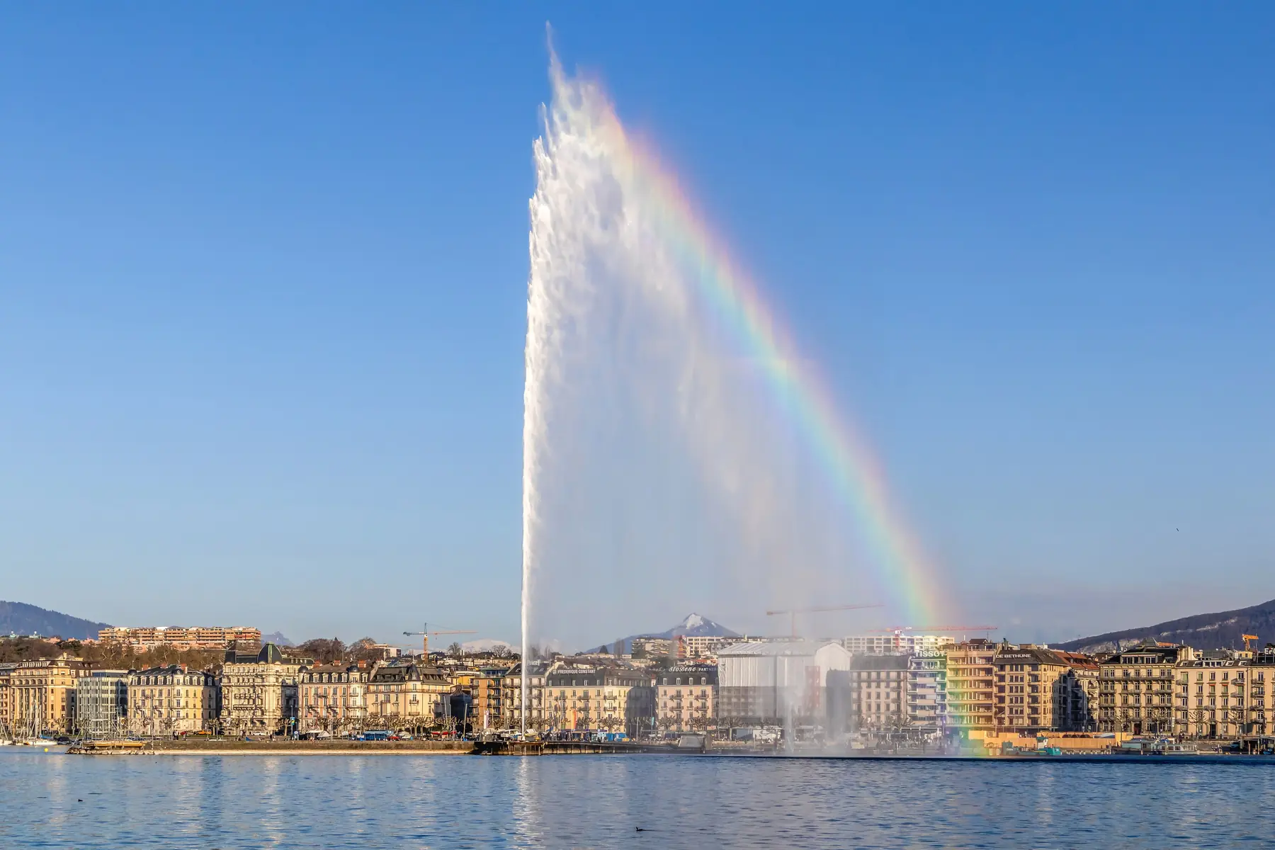 Springvandet Jet d'Eau med en regnbue foran husrækken ved Genèvesøen i Genève