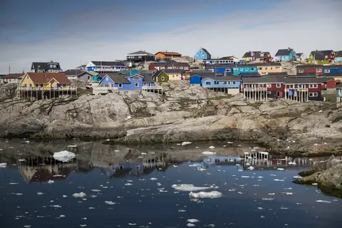 Farverige træhuse på en klippe over vand med drivende isflager i Ilulissat