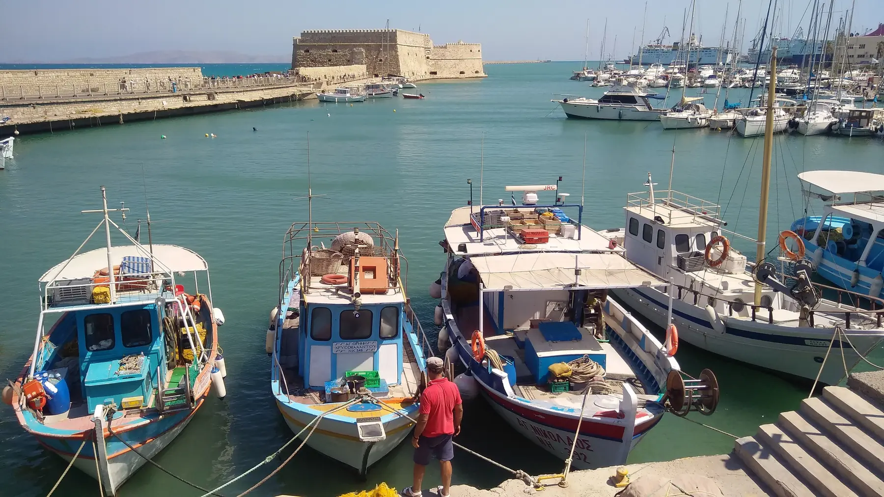 Farverige fiskerbåde i den venetianske havn i Heraklion med fæstningen Koules i baggrunden