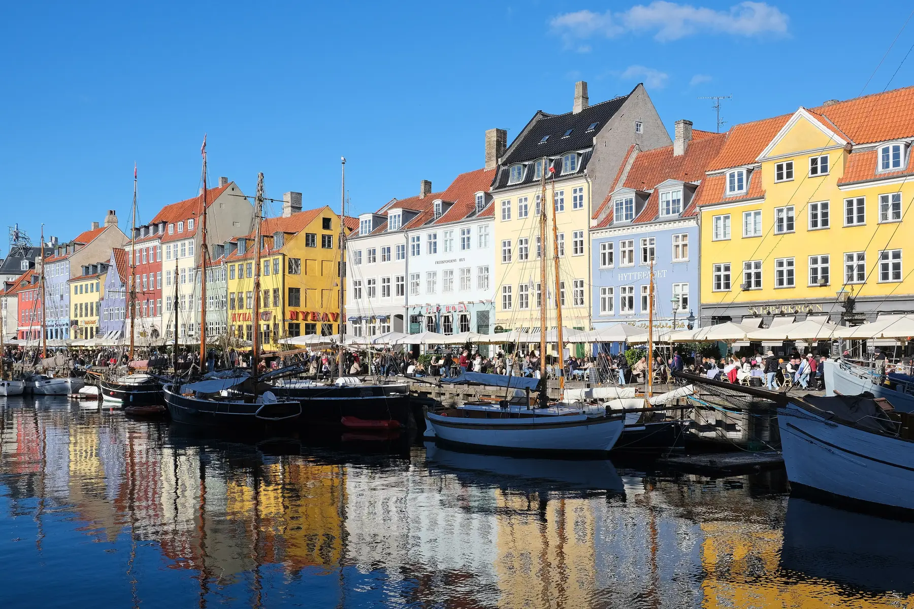 Farverige gavlhuse, udendørsserveringer og træskibe langs kanalen i Nyhavn i København