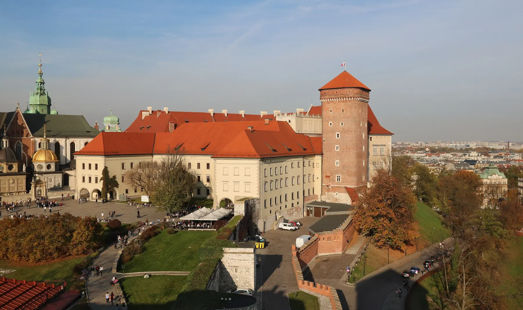 Wawel-slottet med røde tage, Sandomierz-tårnet og katedralens kupler over efterårstræer i Kraków