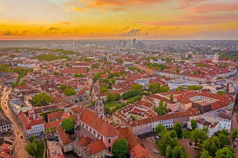 Vilnius' gamle bydel med røde tegltage og kirketårne under en gylden solnedgangshimmel
