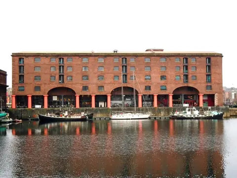Røde murstenspakhuse med søjlegange ved Royal Albert Dock i Liverpool spejlet i havnebassinet