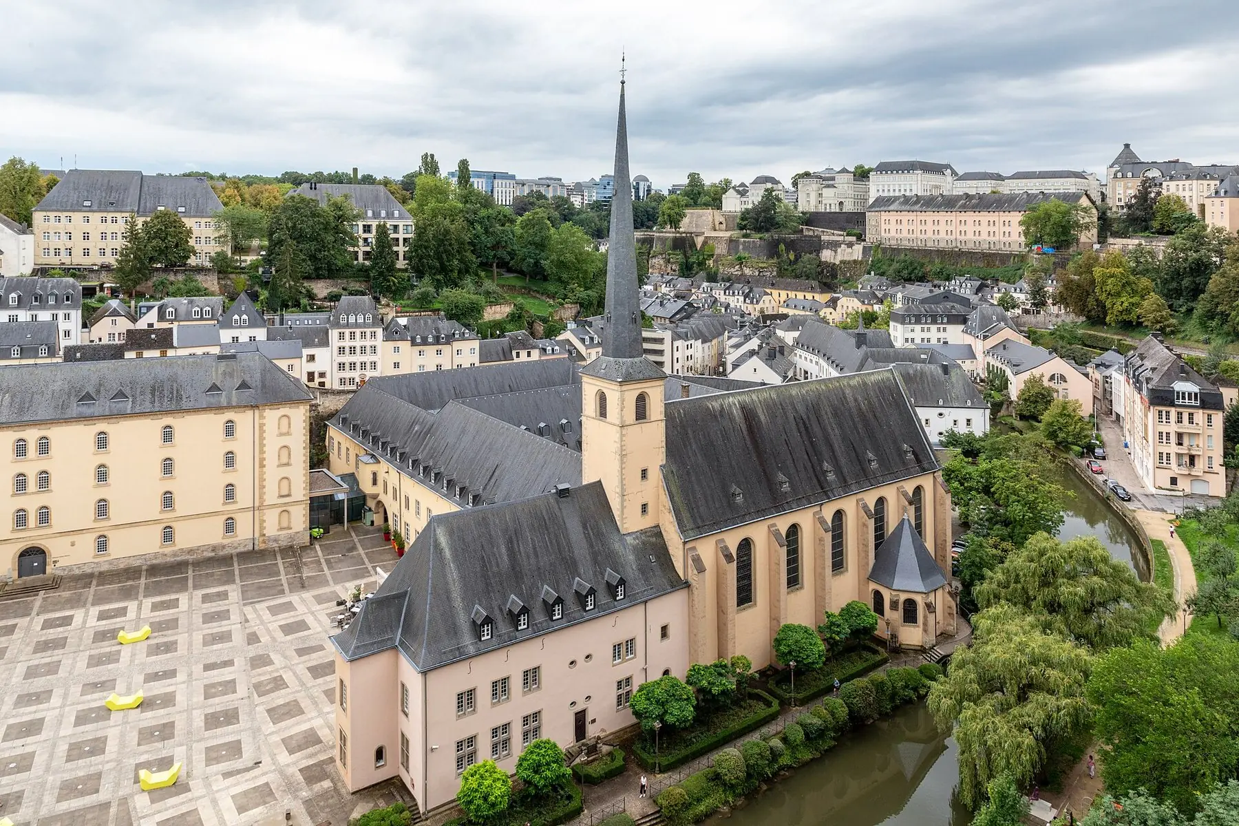 Klosterkirken i bydelen Grund med spidst tårn, omgivet af grønt og gamle huse i Luxembourg by