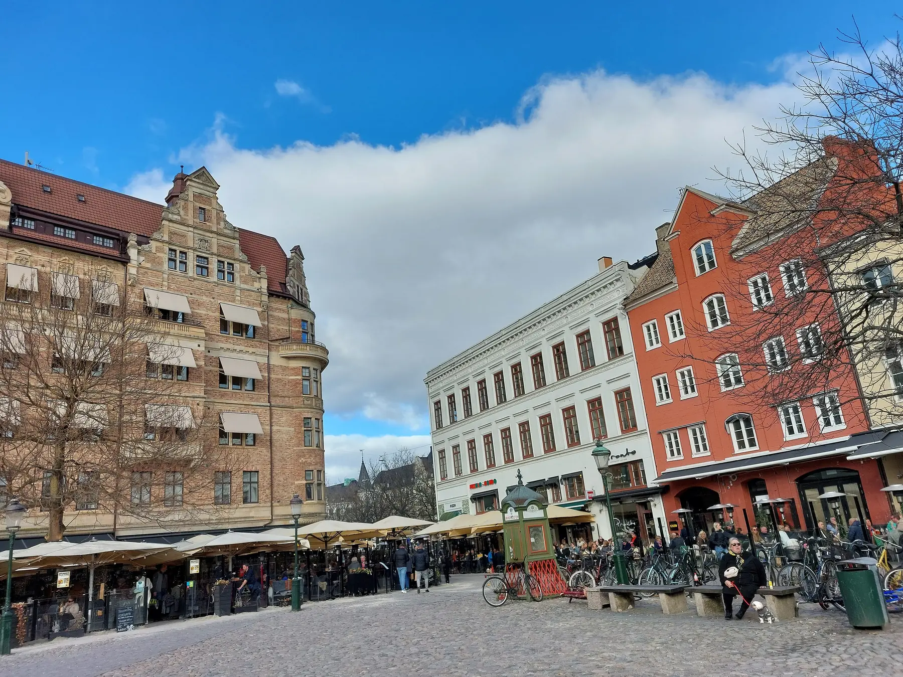 Udendørsserveringer og farverige gamle huse på Lilla Torg i Malmö under blå himmel