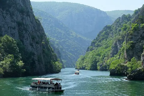 En turistbåd på det grønne vand mellem stejle skovklædte klipper i Matka-kløften uden for Skopje