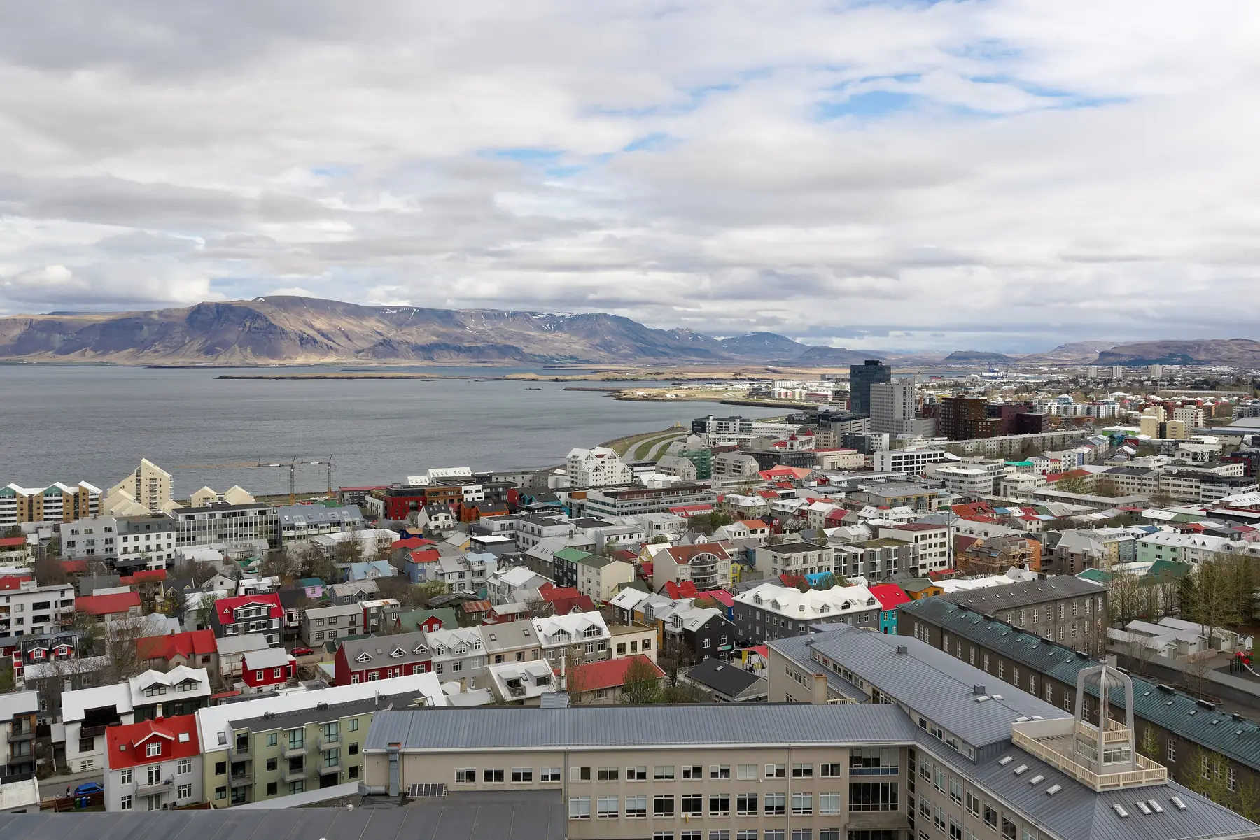 Udsigt over Reykjaviks farverige tage mod havet og bjerget Esja i overskyet vejr