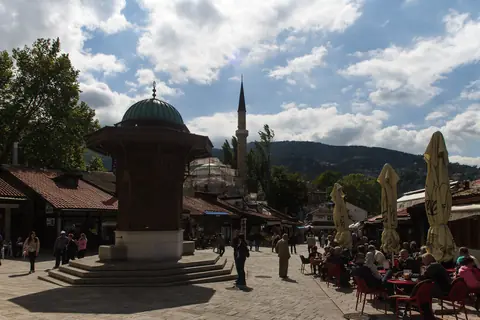 Sebilj-brønden og caféborde på Baščaršija-pladsen i Sarajevo med en minaret bag