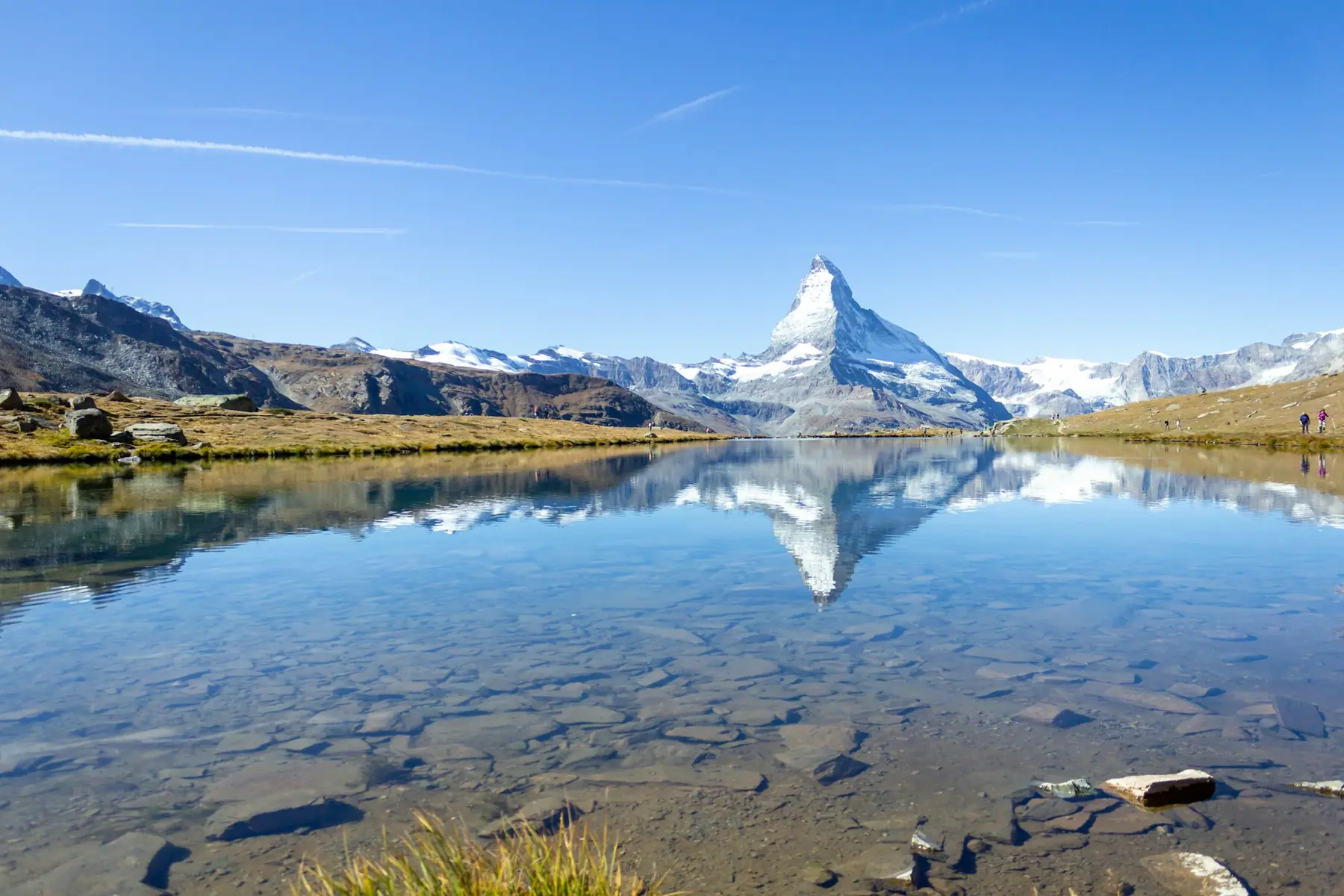 Matterhorn spejler sig i en klar bjergsø ved Zermatt under blå himmel med sneklædte alpetinder