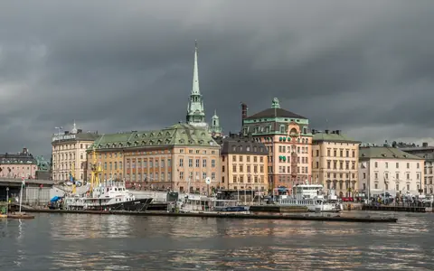 Gamla stan i Stockholm set fra vandet med gamle bygninger, både og et kirkespir under mørke skyer
