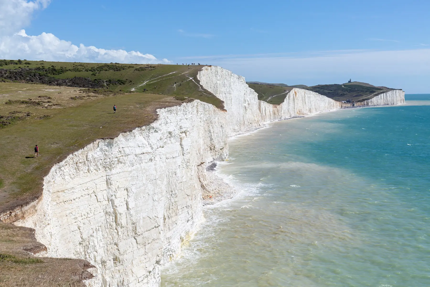 De hvide kridtklinter Seven Sisters ved Den Engelske Kanal i Sussex med vandrere på de grønne skrænter