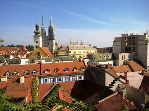 Røde tegltage i Zagreb med katedralens to spir og et kirketårn under blå himmel