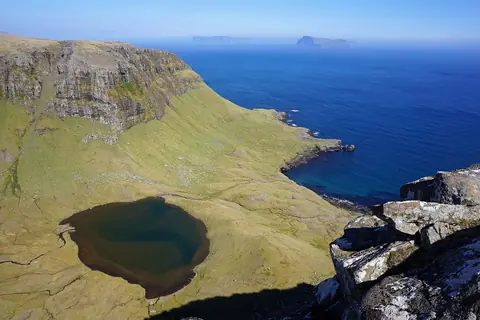 Grønt klippeplateau med en lille sø over et dybblåt hav ved Hvannhagi på Suðuroy