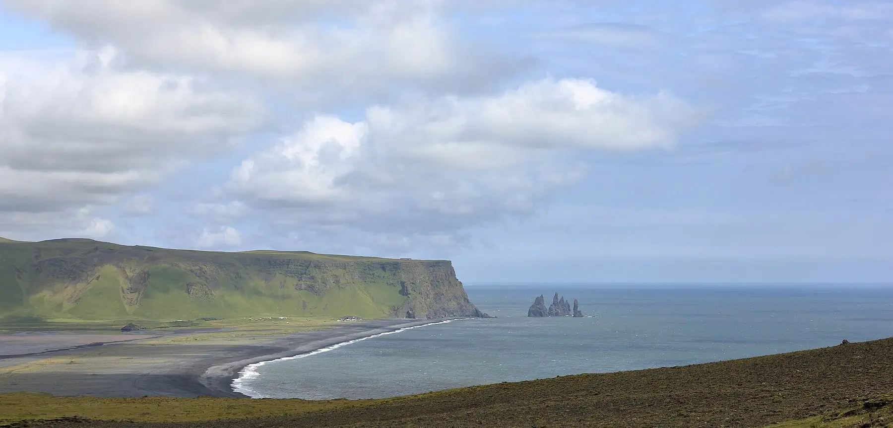 Sort sandstrand og basaltstakke i havet ved Reynisfjara på Islands sydkyst, set fra Dyrhólaey