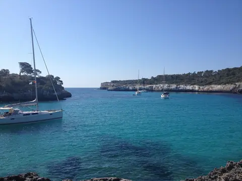Sejlbåde i turkist vand mellem fyrreklædte klipper ved Cala Mondragó på Mallorca